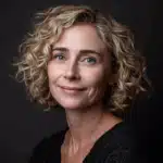 Portrait professionnel d'une femme souriante aux cheveux blonds bouclés, fond sombre, style naturel et chaleureux.